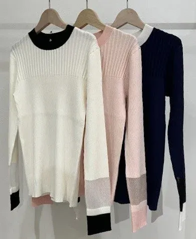 ハンガーにかけられた3枚のリブニットトップス。白、ピンク、ネイビーのセーターは、袖口や襟元に配色デザインが施されており、シンプルながらもスタイリッシュな印象を与えます。