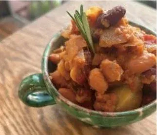 緑色のマグカップに入った、豆と野菜がたっぷり入った具だくさんの煮込み料理