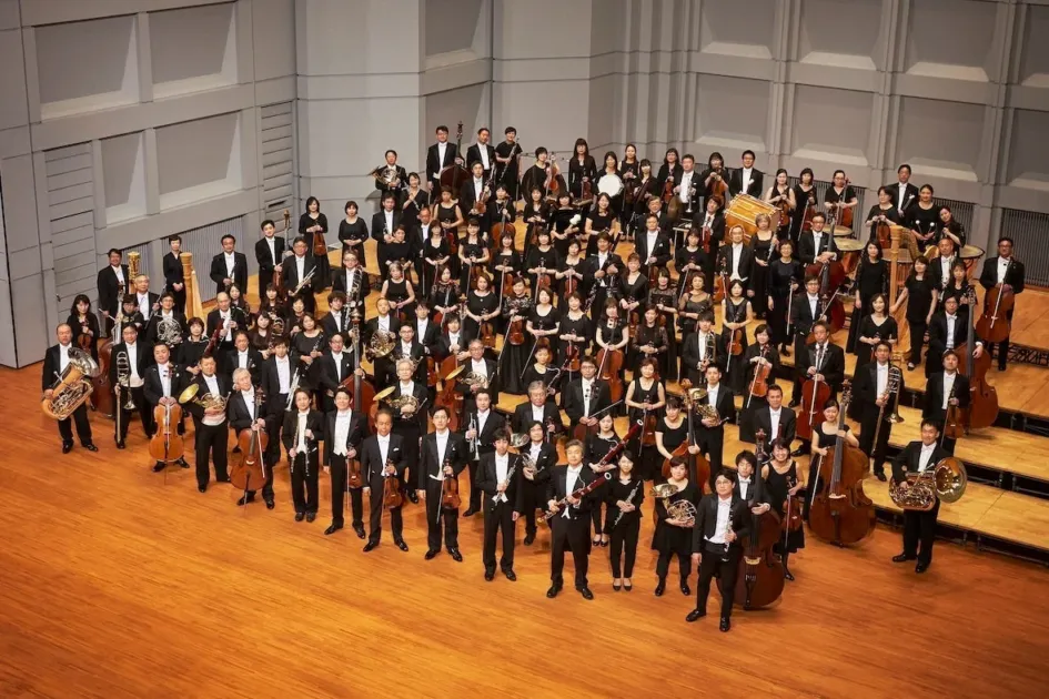 多くの演奏家がステージに集まり、様々な楽器を携えてフォーマルな衣装で並んでいるオーケストラの集合写真