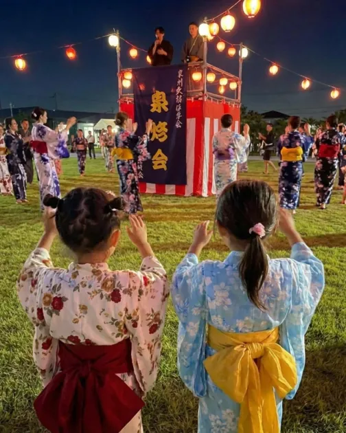 提灯が灯る芝生広場で盆踊りを楽しむ人々