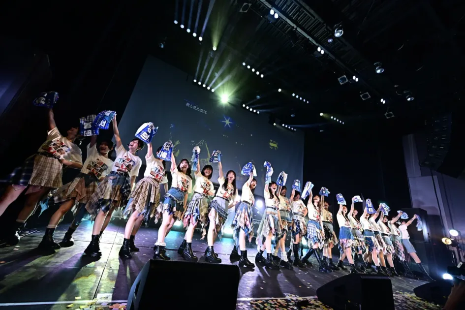 ステージでタオルを掲げパフォーマンスするアイドルグループ