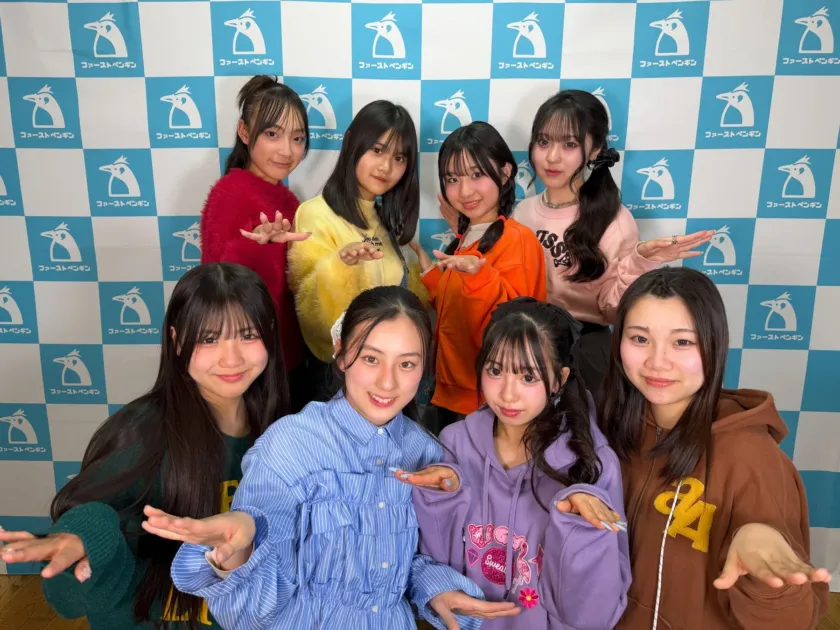 ファーストペンギンのロゴが入った青と白のチェック柄の背景の前で、8人の若い女性が笑顔でポーズをとっている集合写真