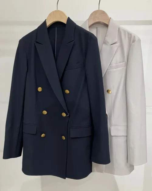 ハンガーにかけられたネイビーとライトグレーのダブルブレストジャケット。金色のボタンが特徴で、ビジネスからカジュアルまで幅広いシーンで活躍しそうなアウターです。