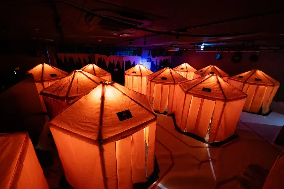 暗い屋内に複数のオレンジ色のテントのような構造物が並び、内部から暖かく光を放っています。幻想的で落ち着いた雰囲気のイベント会場や休憩スペースを思わせる光景です。