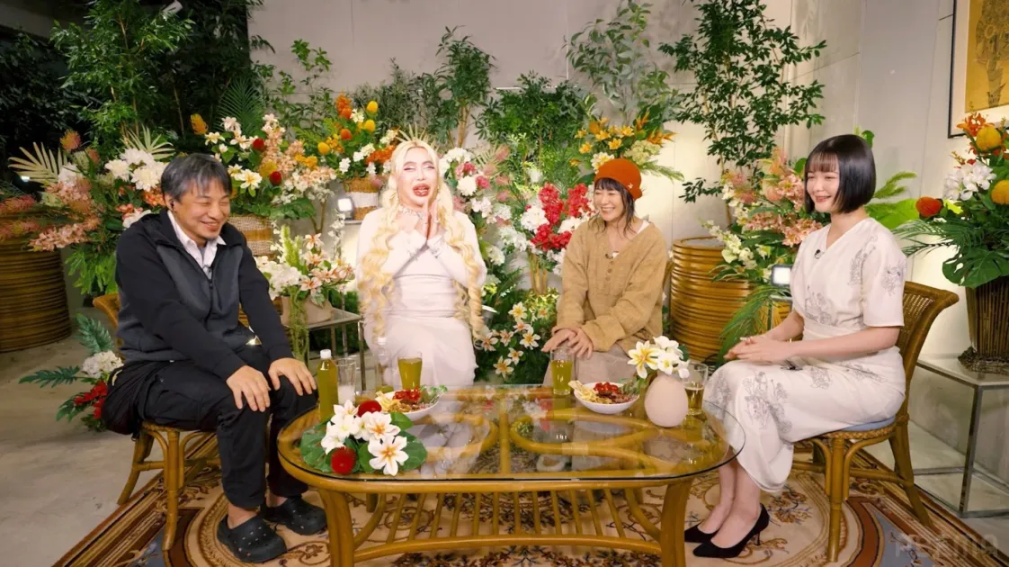 花と植物で装飾されたスタジオで4人の男女が笑顔で会話する様子