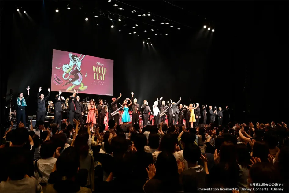 ステージ上で演奏者が観客に手を振っているコンサートの様子