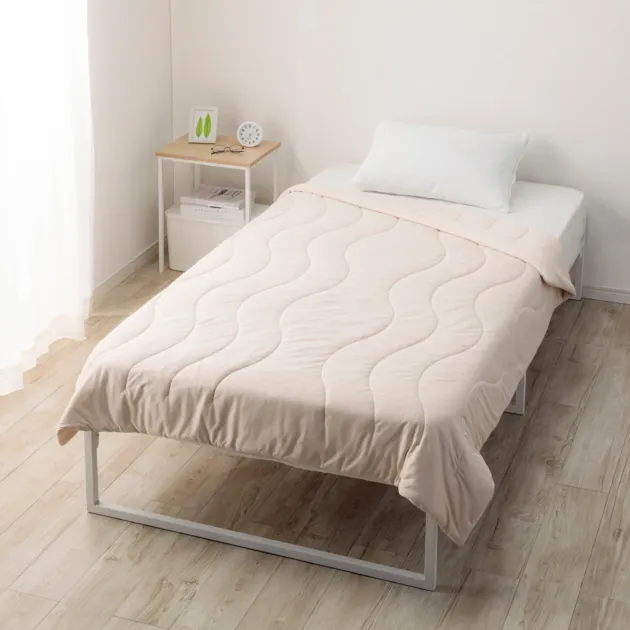 ベージュ系の掛け布団と白い枕が整えられたシンプルなシングルベッド