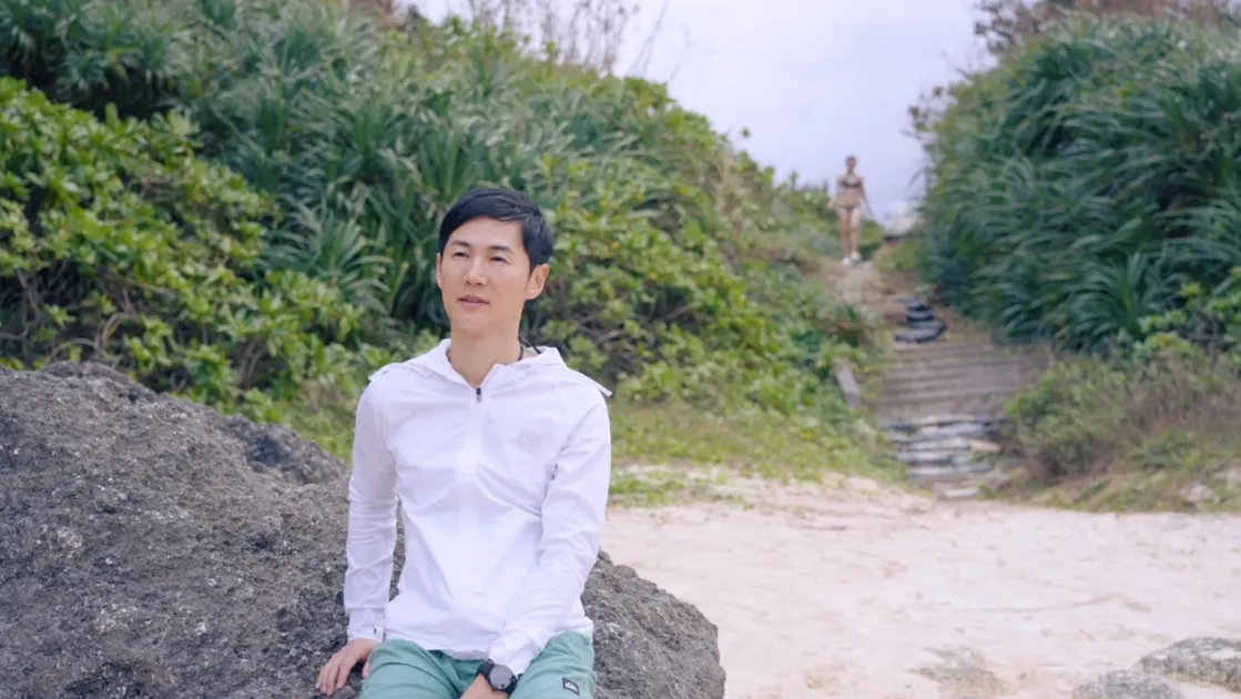 ビーチで男性が岩に座り、女性が奥の小道を歩く様子