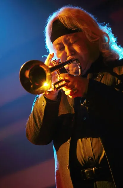 長い金髪の男性ミュージシャンがトランペットを演奏