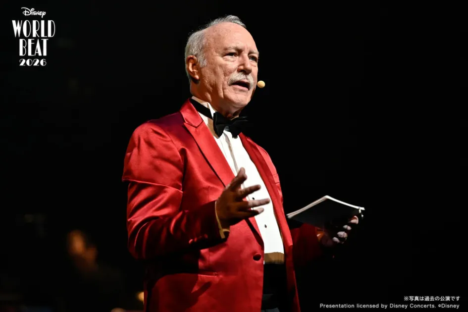 赤いタキシードの男性がステージでプレゼンテーションを行っている様子