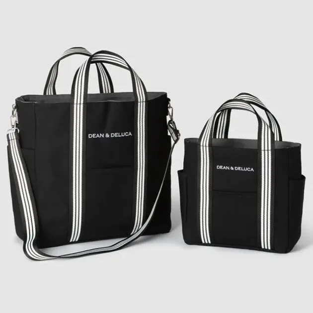 大小2つのDEAN & DELUCAのブラックトートバッグが写っています。白いストライプの持ち手とロゴが特徴で、大きい方にはショルダーストラップも付いています。