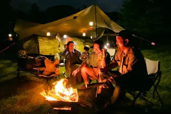 夜のキャンプ場で、数人の仲間が焚き火を囲んで談笑し、楽しんでいる様子