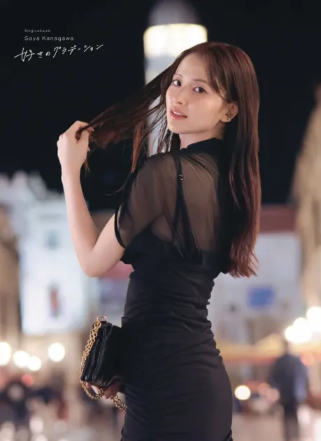 夜の街を背景に、黒いドレスをまとった乃木坂46の金川紗耶さんが振り返り、カメラを見つめています。髪に手を添えたポーズが印象的で、エレガントな雰囲気が漂うポートレートです。