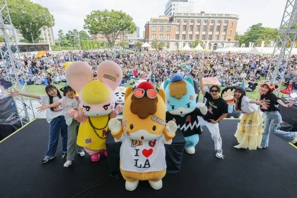 屋外イベントのステージで、複数のマスコットキャラクターとパフォーマーたち