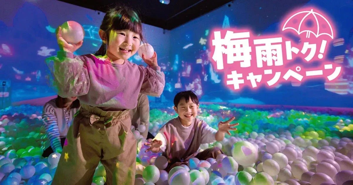 カラフルなボールプールで楽しそうに遊ぶ子供たちの様子を捉えた画像です。背景には「梅雨トク! キャンペーン」という文字と傘のイラストが投影されており、雨季のイベントを告知しているようです。