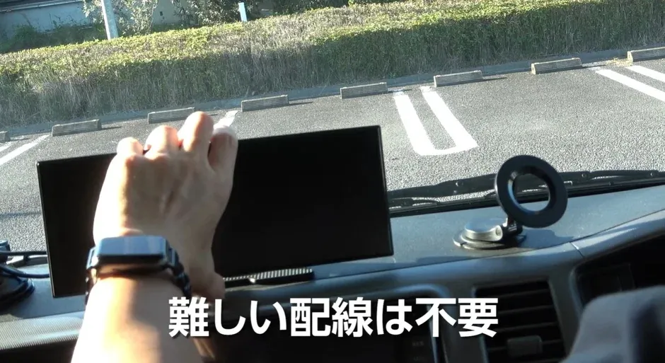 車のダッシュボードに設置されたデバイスを調整する手元が写っています。背景は駐車場で、「難しい配線は不要」というテキストが表示されており、簡単な取り付けをアピールしているようです。