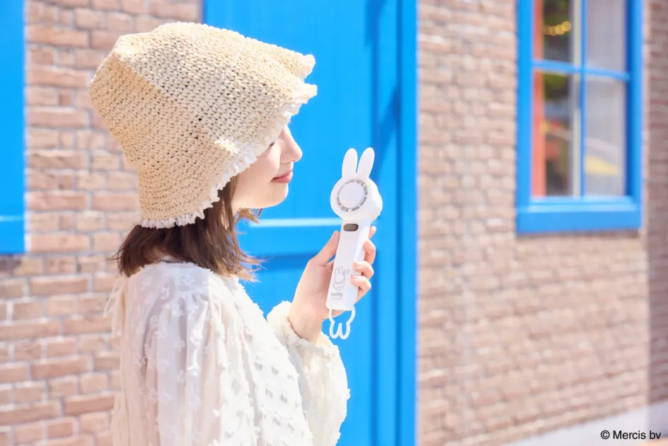麦わら帽子をかぶった女性が、ミッフィーデザインのハンディファンで涼んでいる様子