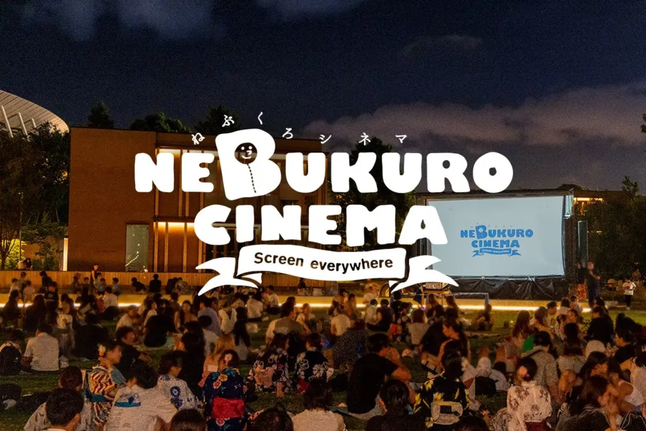 夜の屋外で多くの人々が芝生に座り、大きなスクリーンで映画を鑑賞する様子