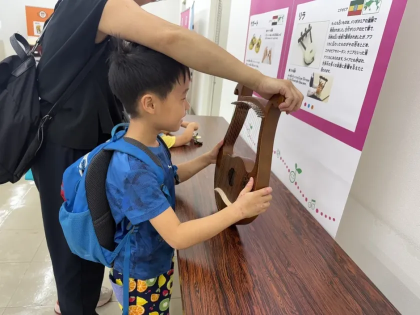 展示会場でリラのような弦楽器に触れて興味を示す子供