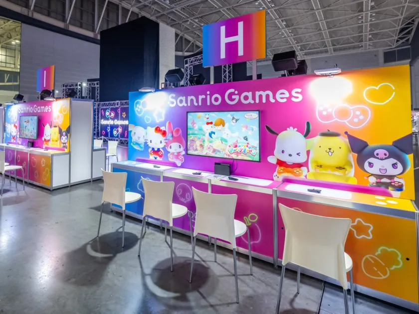 サンリオキャラクターのゲームが体験できる展示ブースの様子。ハローキティやポムポムプリンなどの人気キャラクターが描かれたカラフルな空間で、来場者がゲームを楽しめるよう複数のプレイステーションと椅子が設置されています。