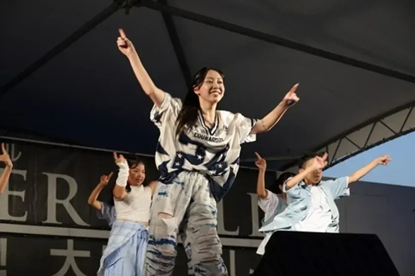 ステージ上で笑顔で両腕を上げて踊る若い女性