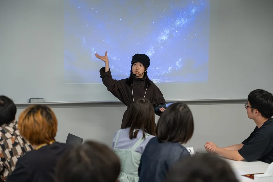 女性がヘッドセットマイクを装着し、星空が映し出されたプロジェクターの前でプレゼンテーションを行っています