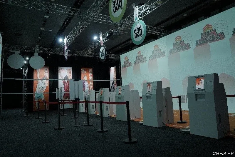 アニメ『ハイキュー!!』の屋内イベント会場で、キャラクターパネルやインタラクティブな装置が並び、「目指せ! 最高到達点!!」の文字が投影されている