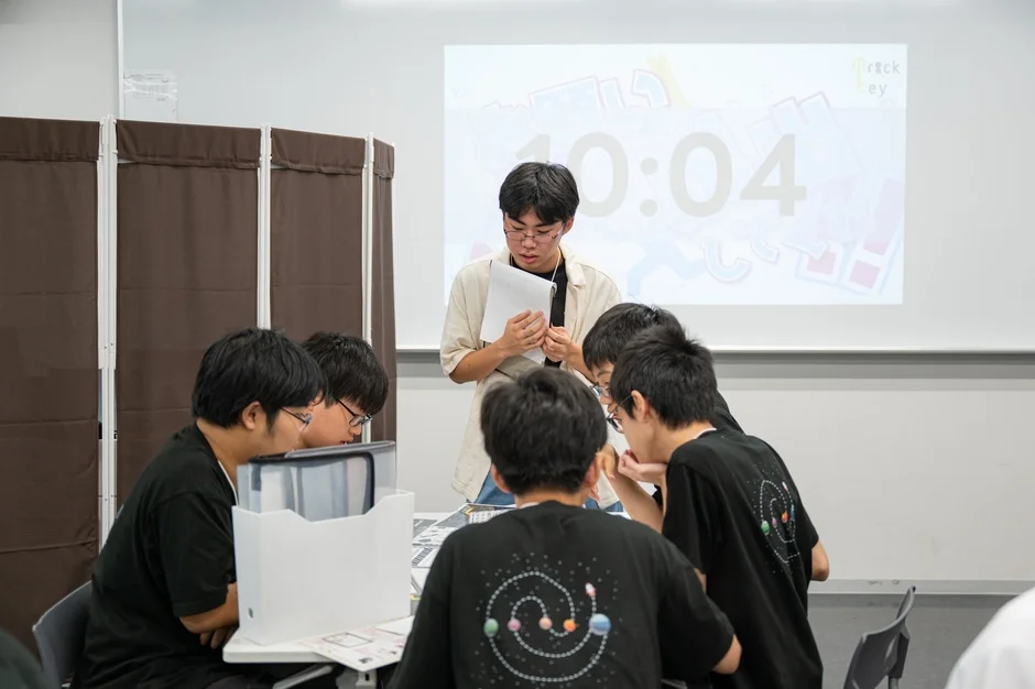 複数の学生が教室で集まり、プロジェクターに映し出されたタイマーを見ながらグループディスカッションや勉強会を行っている様子