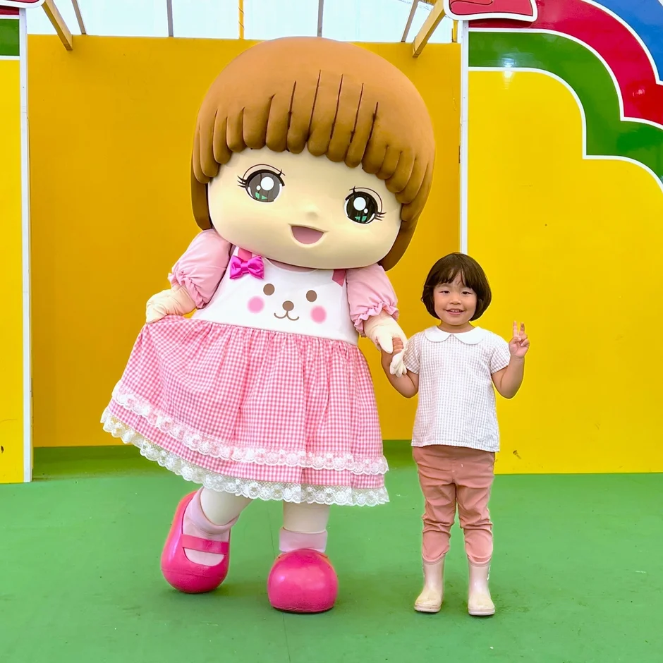 大きなマスコットキャラクターと小さな女の子が手をつないで笑顔で立っている。