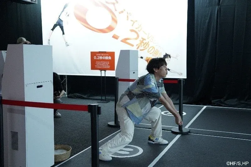 男性がアニメ『ハイキュー!!』をテーマにしたインタラクティブなイベントに参加しており、バレーボールのレシーブのような姿勢をとっている