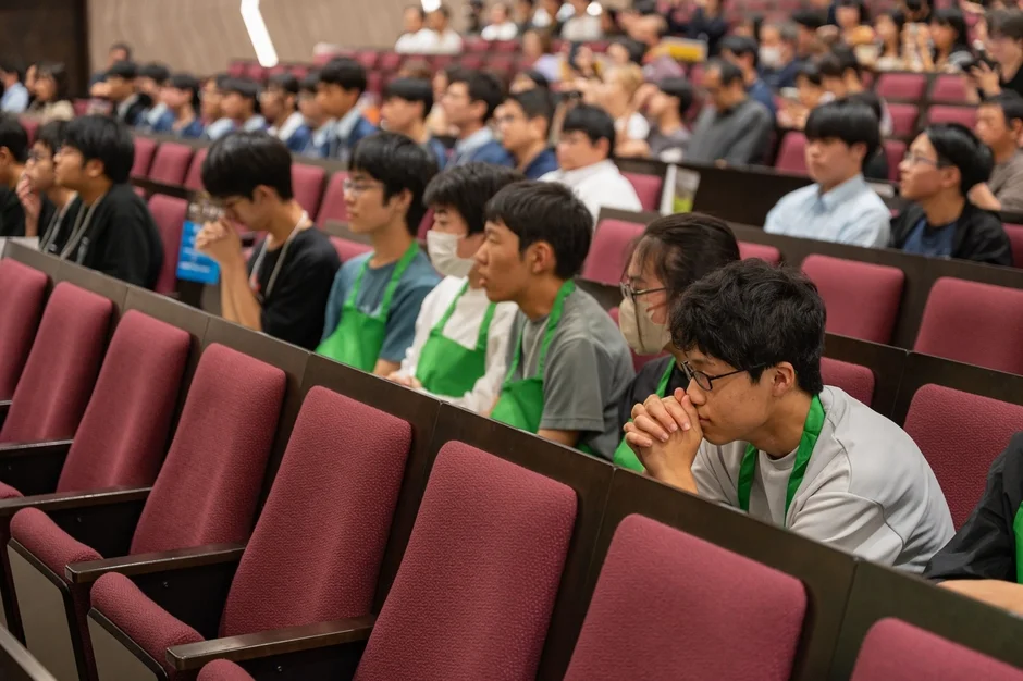 講堂で講演やプレゼンテーションを熱心に聞いている多くの学生や若者たちの様子