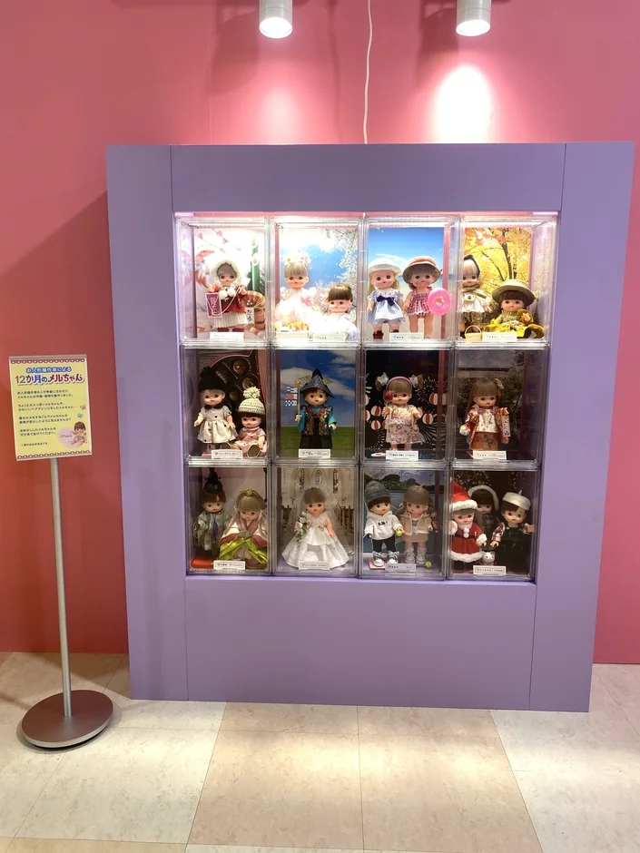 ピンクの壁を背景に、紫色のショーケースに「12か月のメルちゃん」が展示されています。