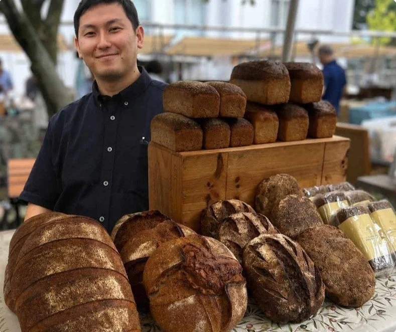屋外の市場で、笑顔の男性が手作りのパンを販売しています。