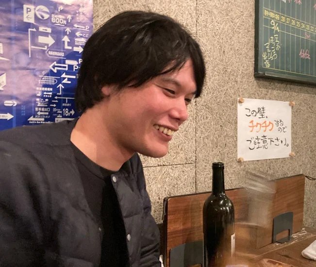 笑顔の男性が居酒屋のようなカジュアルな店内でリラックスした表情を見せています。