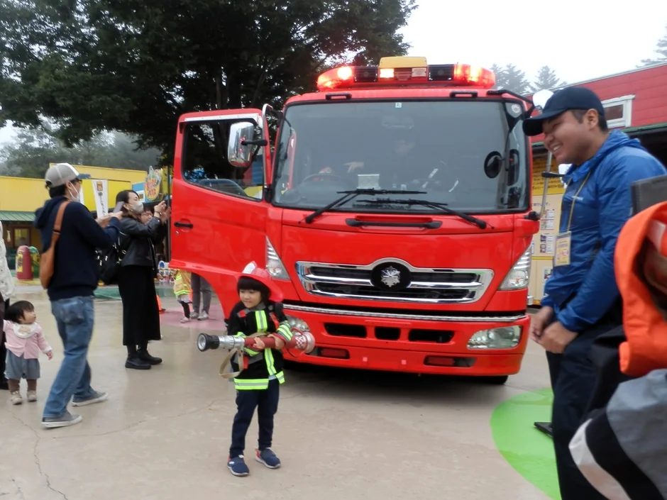 消防士の制服を着た子どもがホースを持ってポーズを取っています。