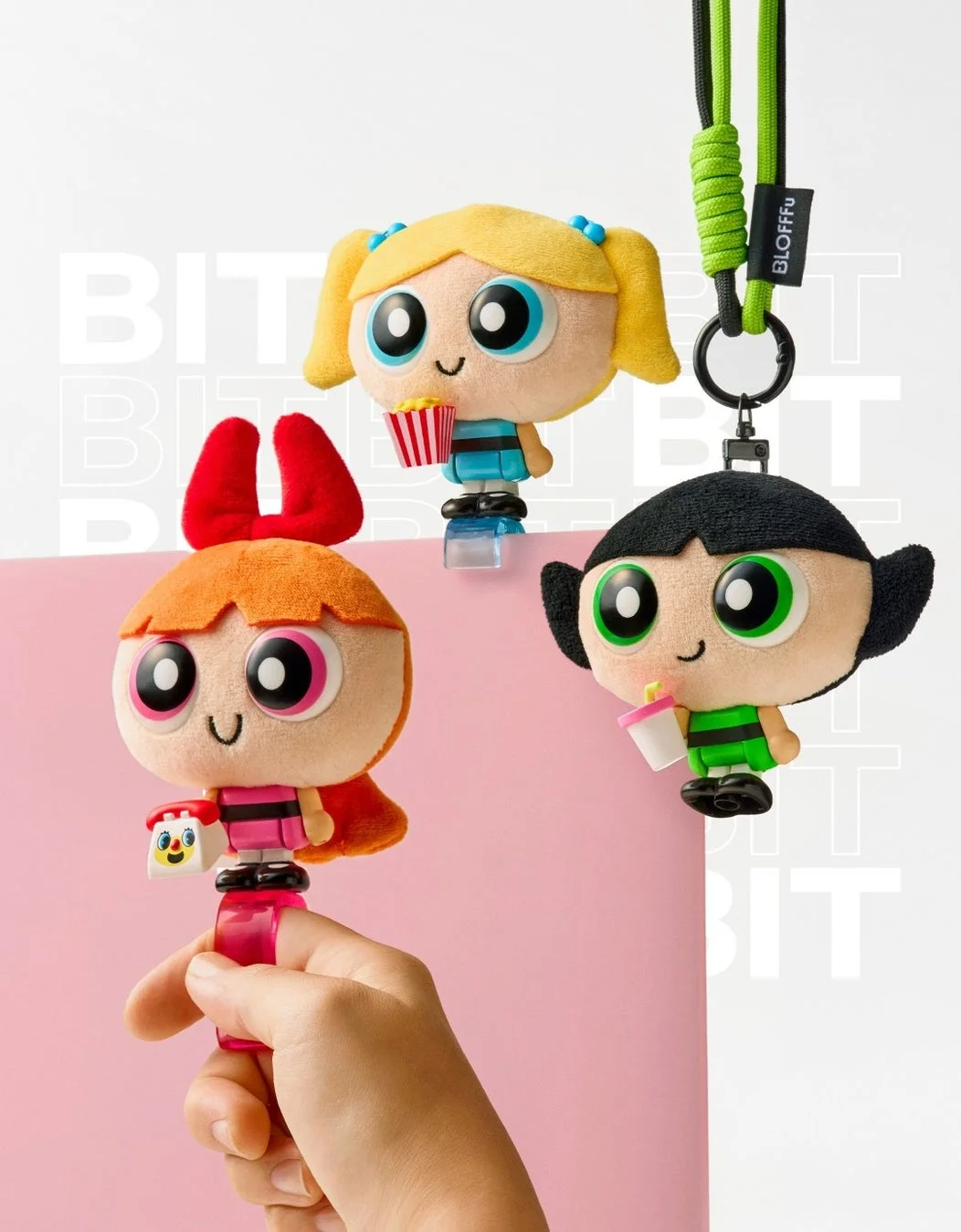パワーパフガールズのぬいぐるみキーホルダー3体が写っています。ブロッサムが手に持たれており、バブルスはポップコーン、バターカップはドリンクを持っています。背景はピンクと白です。