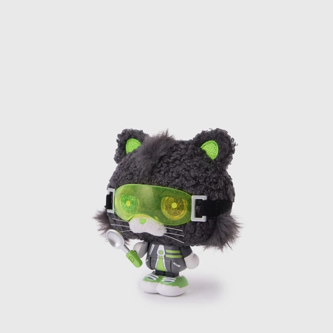 緑色のゴーグルをかけた黒い猫のキャラクターぬいぐるみ（またはフィギュア）が、小さなスプーンを持っている様子。背景は白一色で、キャラクターが際立っています。